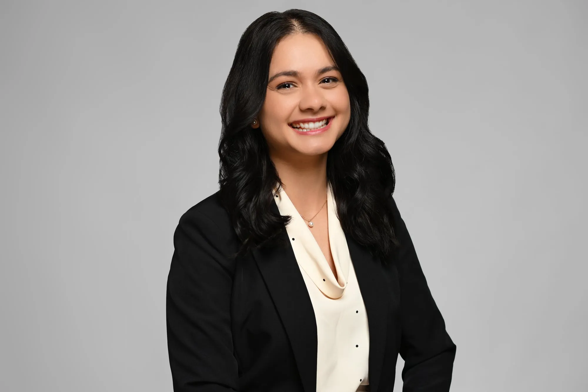 ERAS-ready medical residency headshot: black blazer and cream blouse, grey background