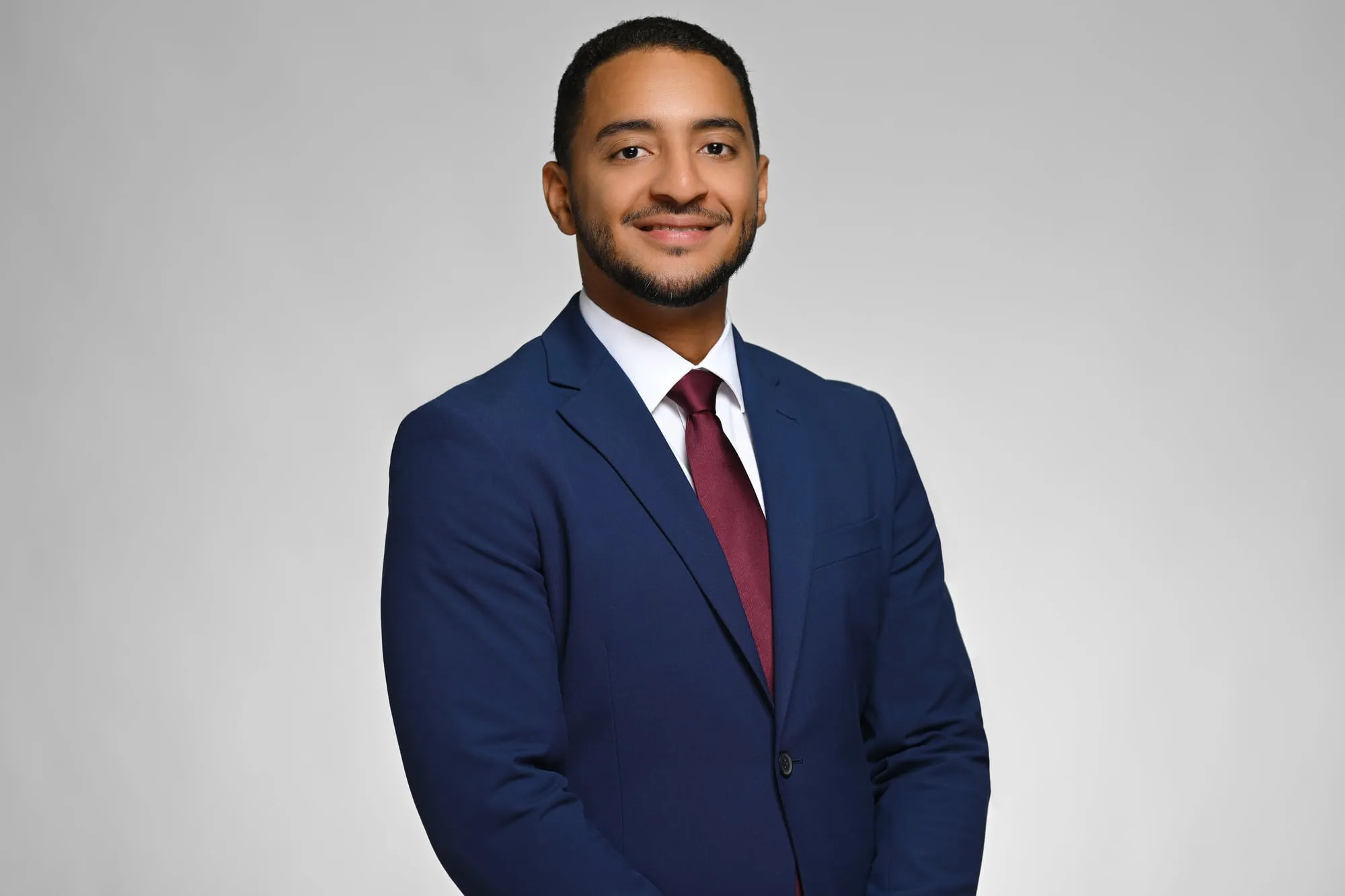 ERAS-ready medical residency headshot: navy suit and burgundy tie, grey background
