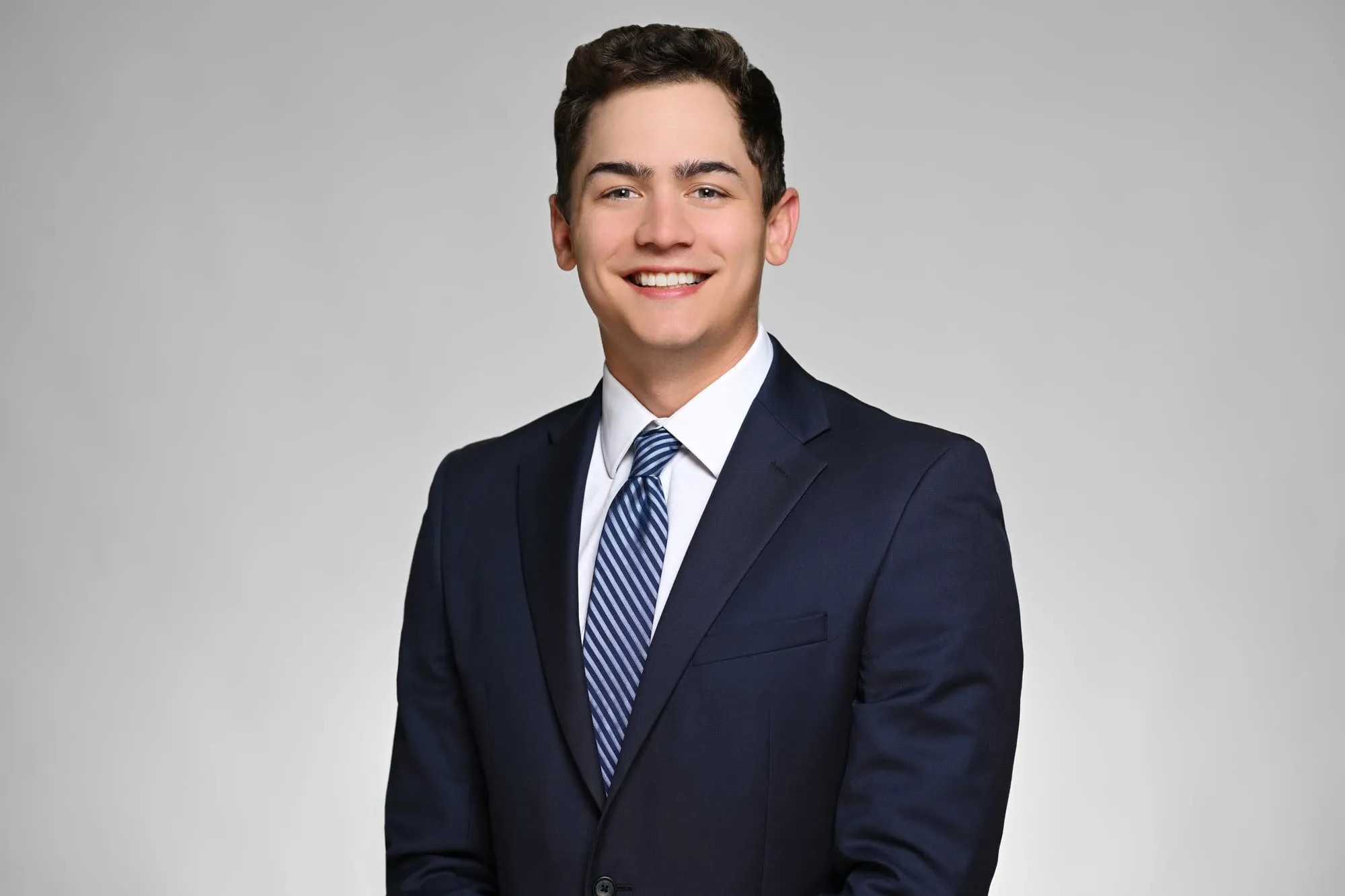 ERAS-ready medical residency headshot: navy suit and blue striped tie, grey background