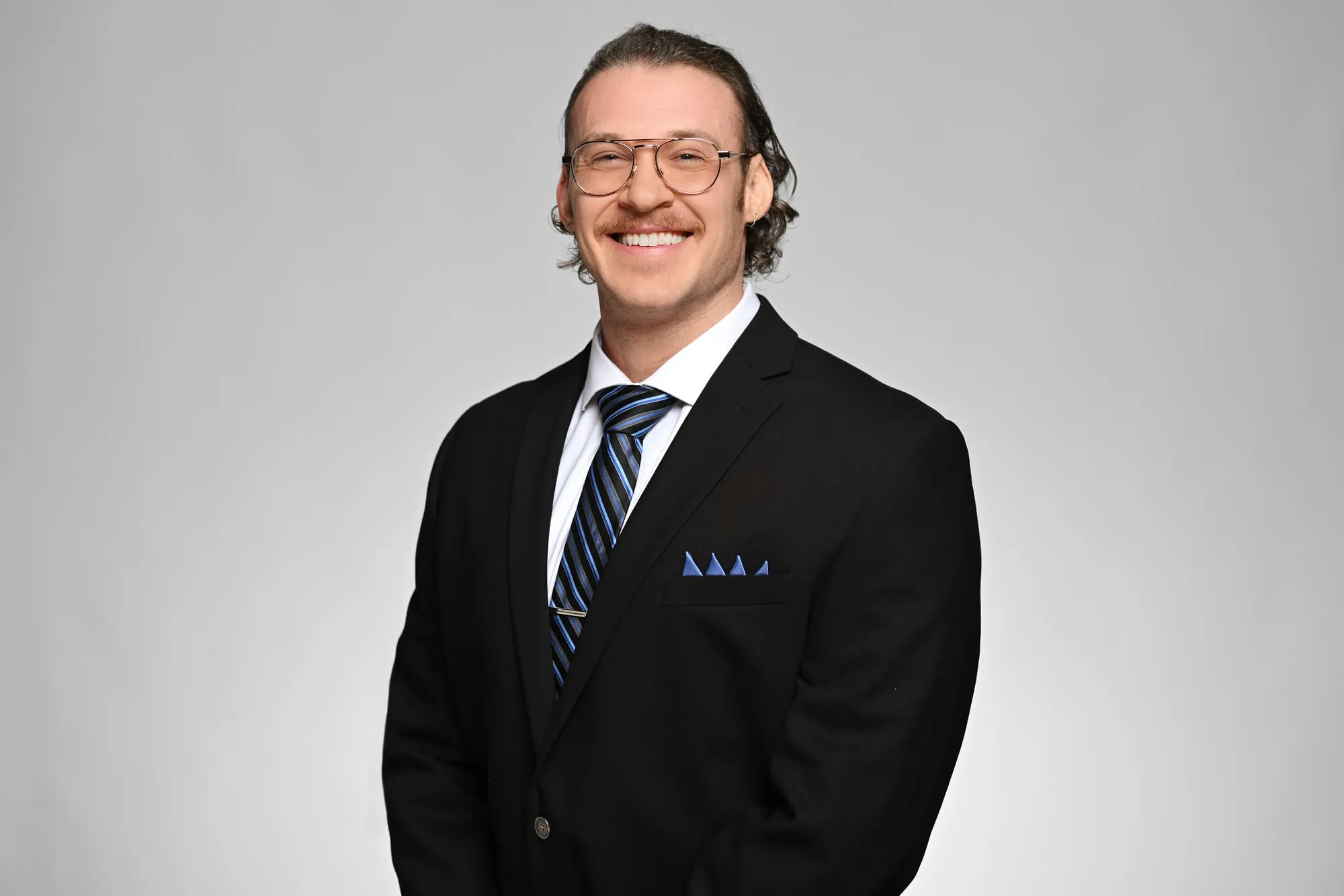 ERAS-ready medical residency headshot: black suit, glasses, and pocket square, grey background