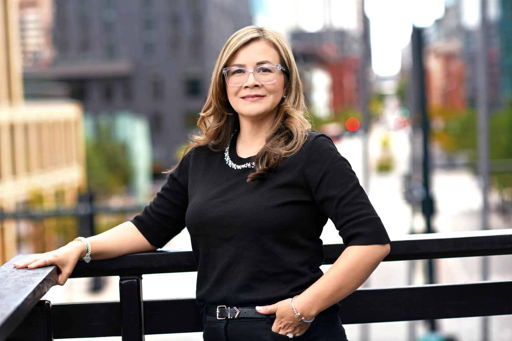 On-location headshot in Denver: black dress, leaning on a railing with a downtown street behind