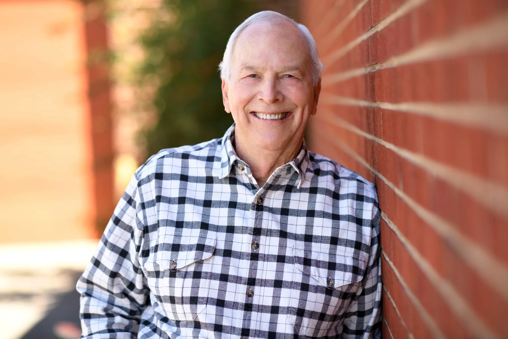 On-location headshot in Denver: plaid shirt, leaning on a sunlit brick wall