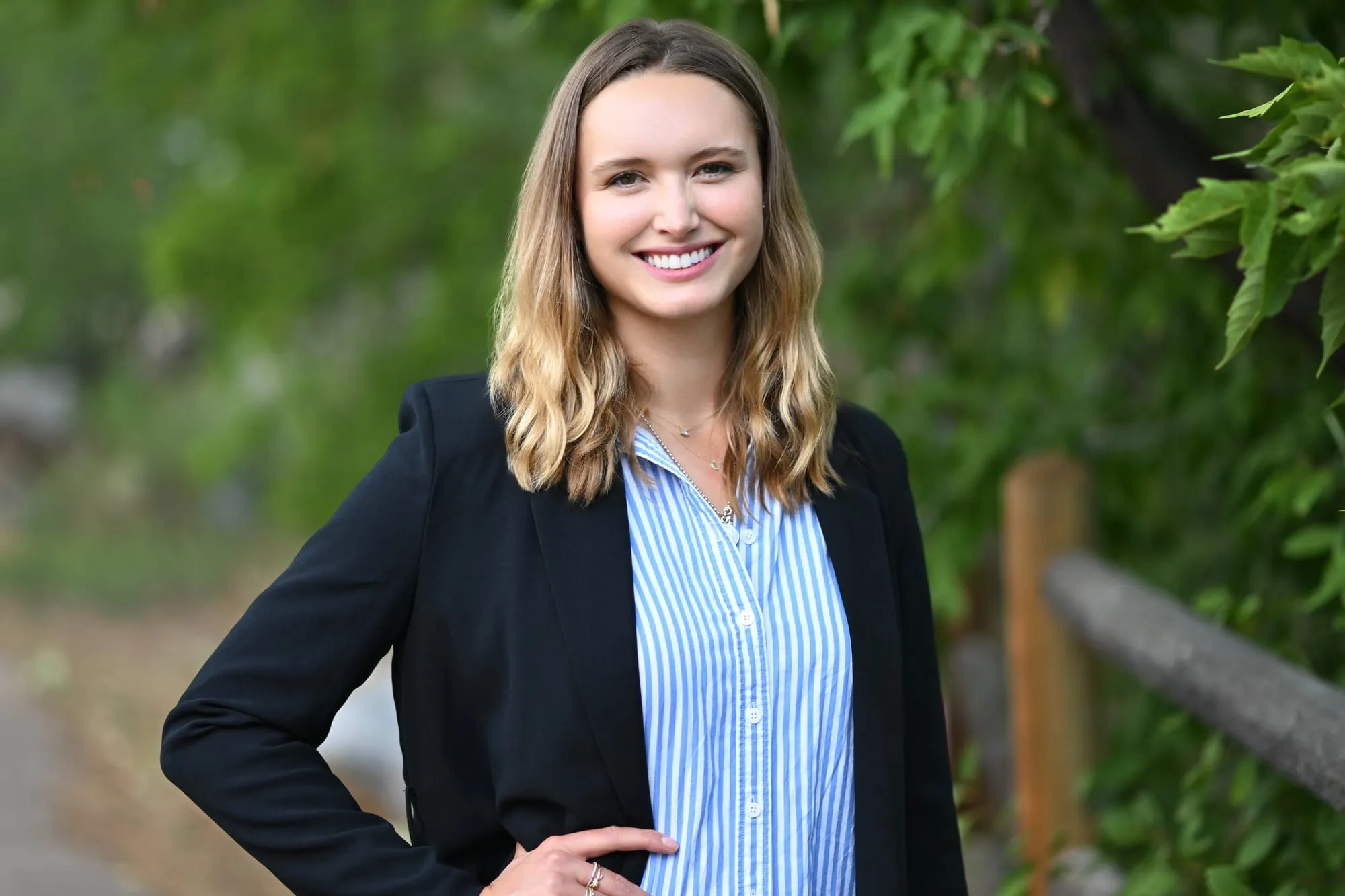 On-location headshot in Denver: black blazer and blue striped shirt against green foliage