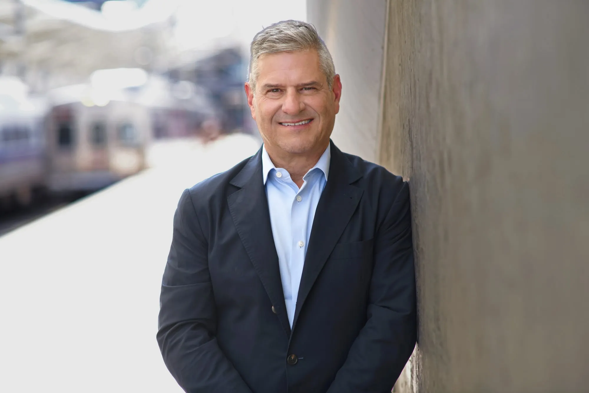 On-location headshot in Denver: dark blazer, leaning on a concrete wall with the city behind