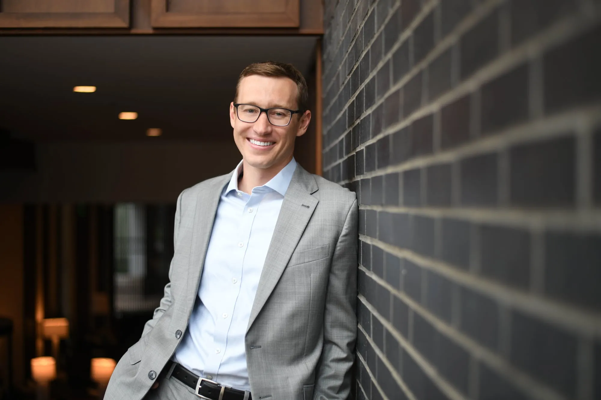 On-location headshot in Denver: grey blazer, leaning on a dark brick wall