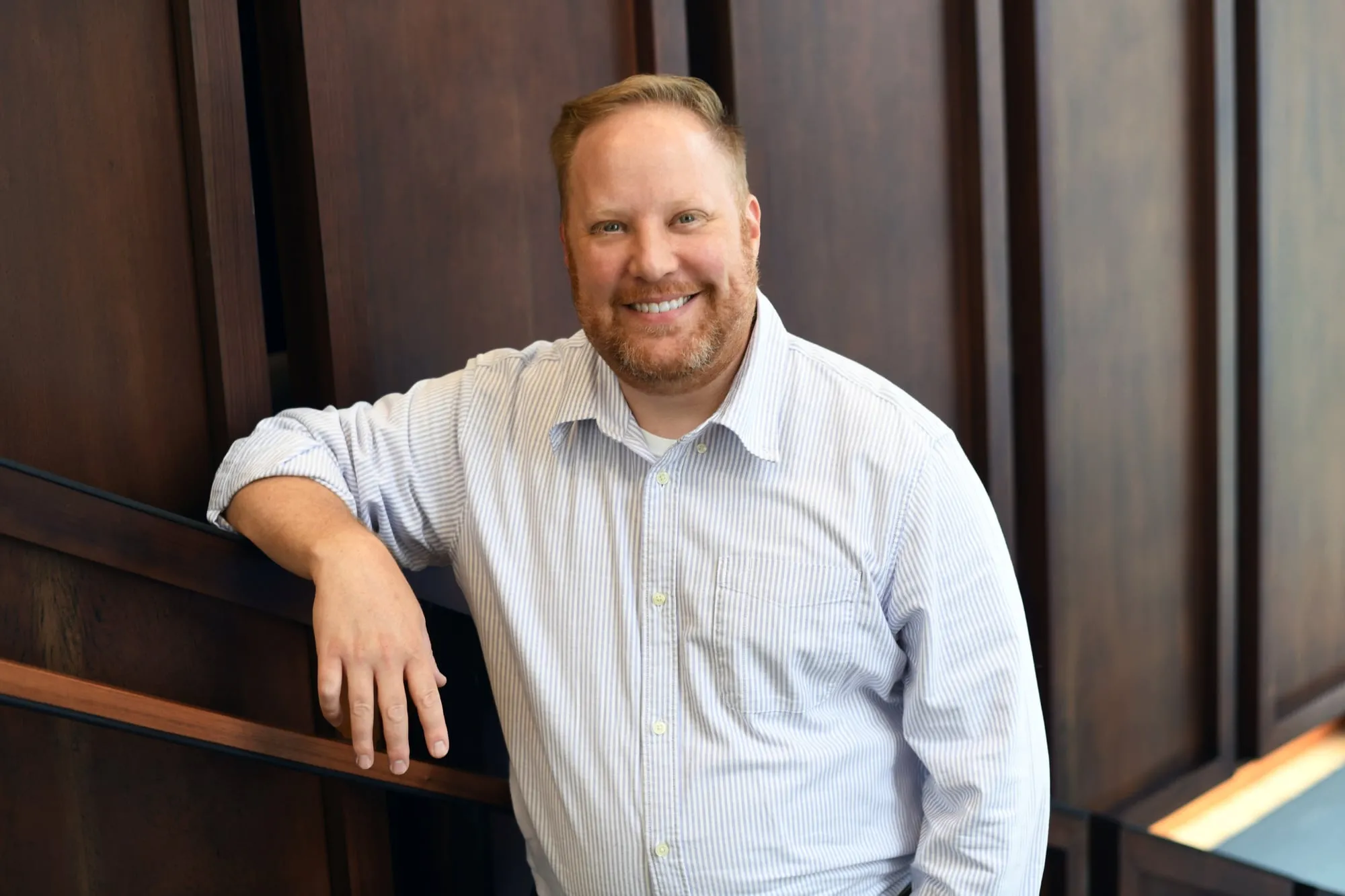 On-location headshot in Denver: light button-up shirt, leaning on wood paneling