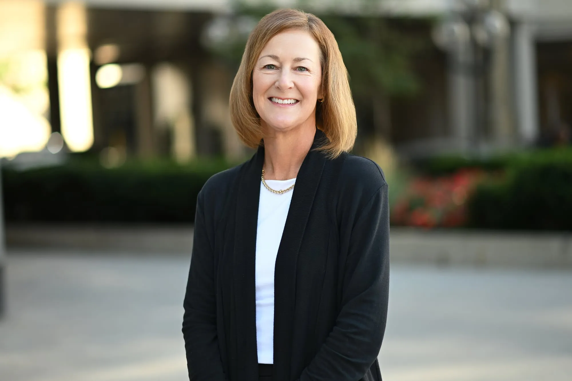 On-location headshot in Denver: black cardigan in a tree-lined plaza