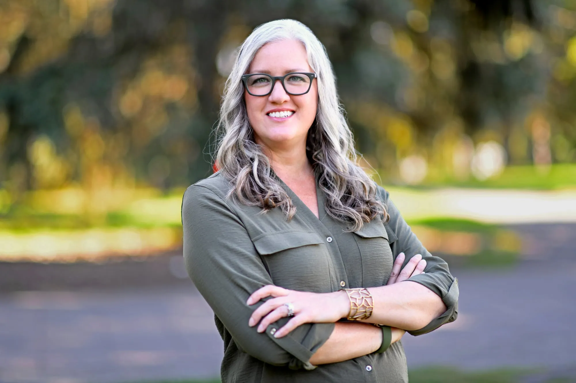 On-location headshot in Denver: olive shirt and glasses, arms crossed, in a park at golden hour