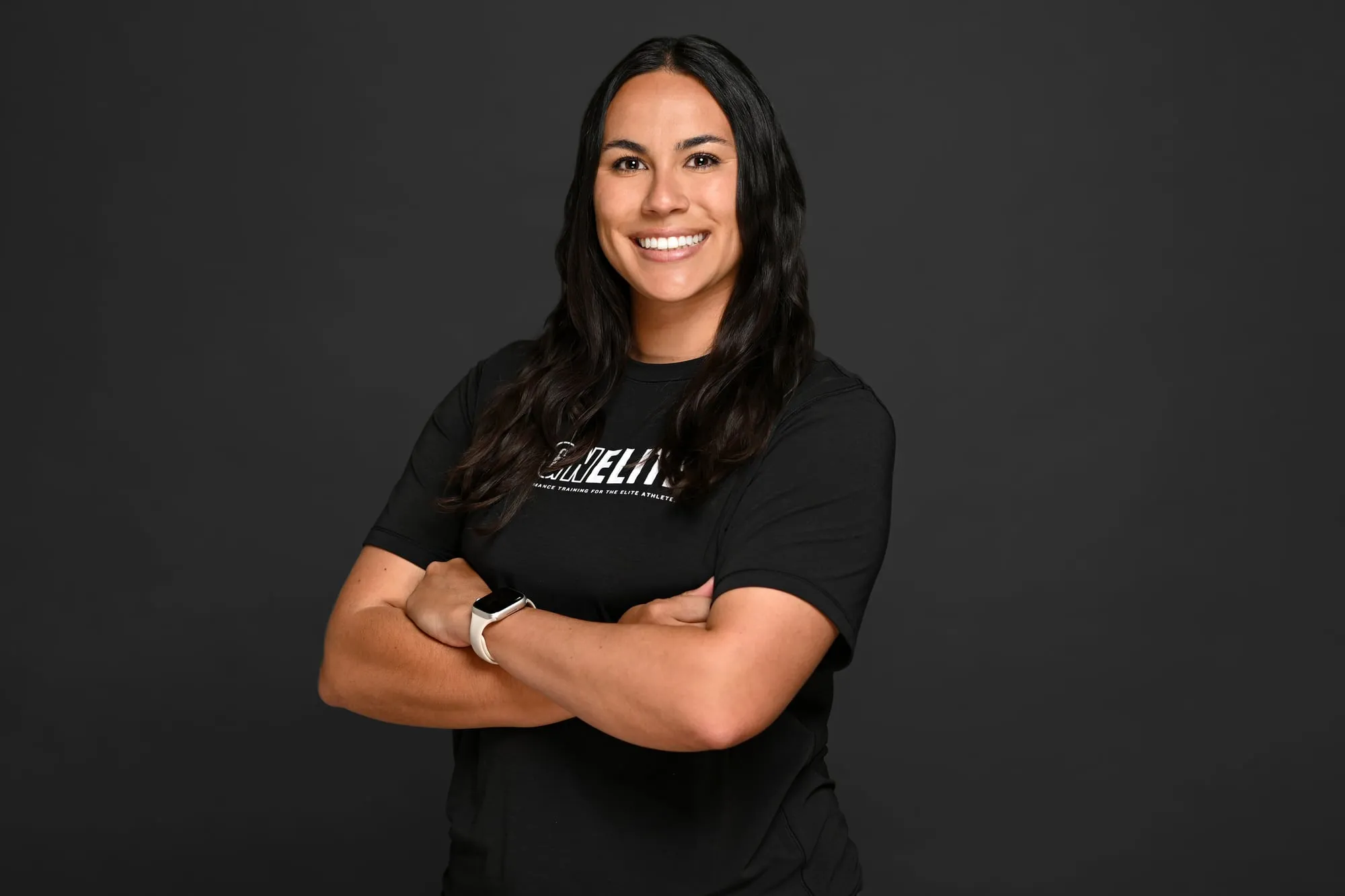 Studio headshot on a black background: black athletic tee, arms crossed