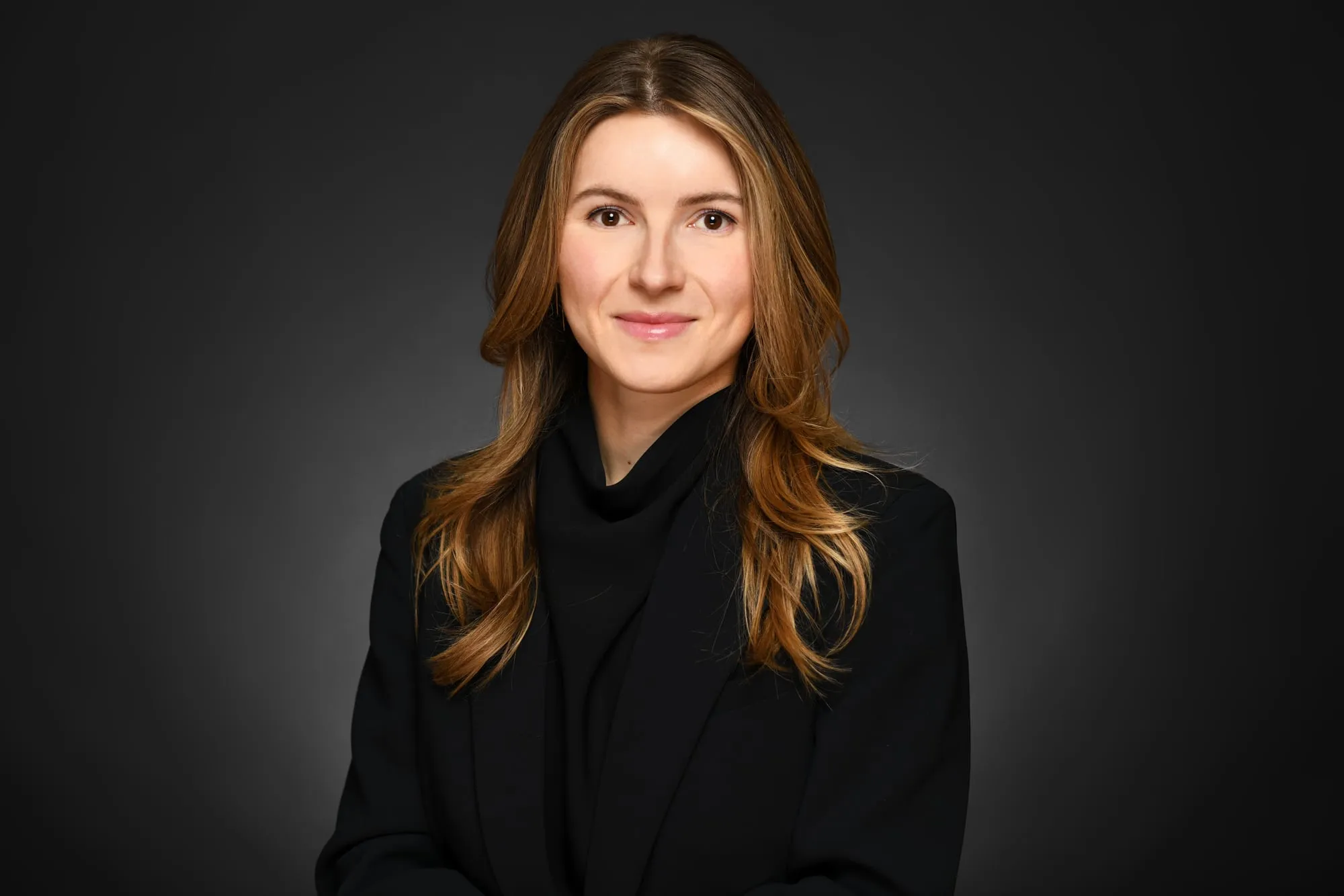 Studio headshot on a black background: black top and long wavy hair