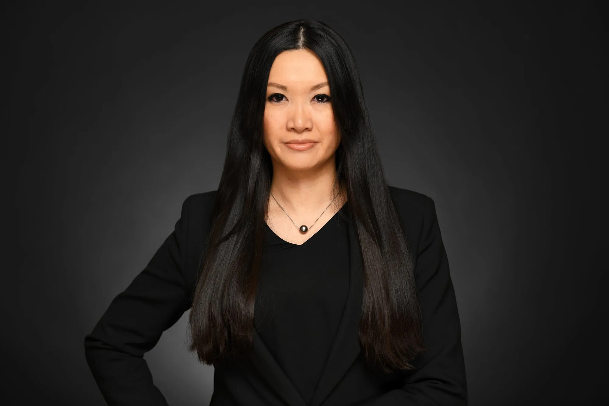 Studio headshot on a black background: black blazer and long straight hair