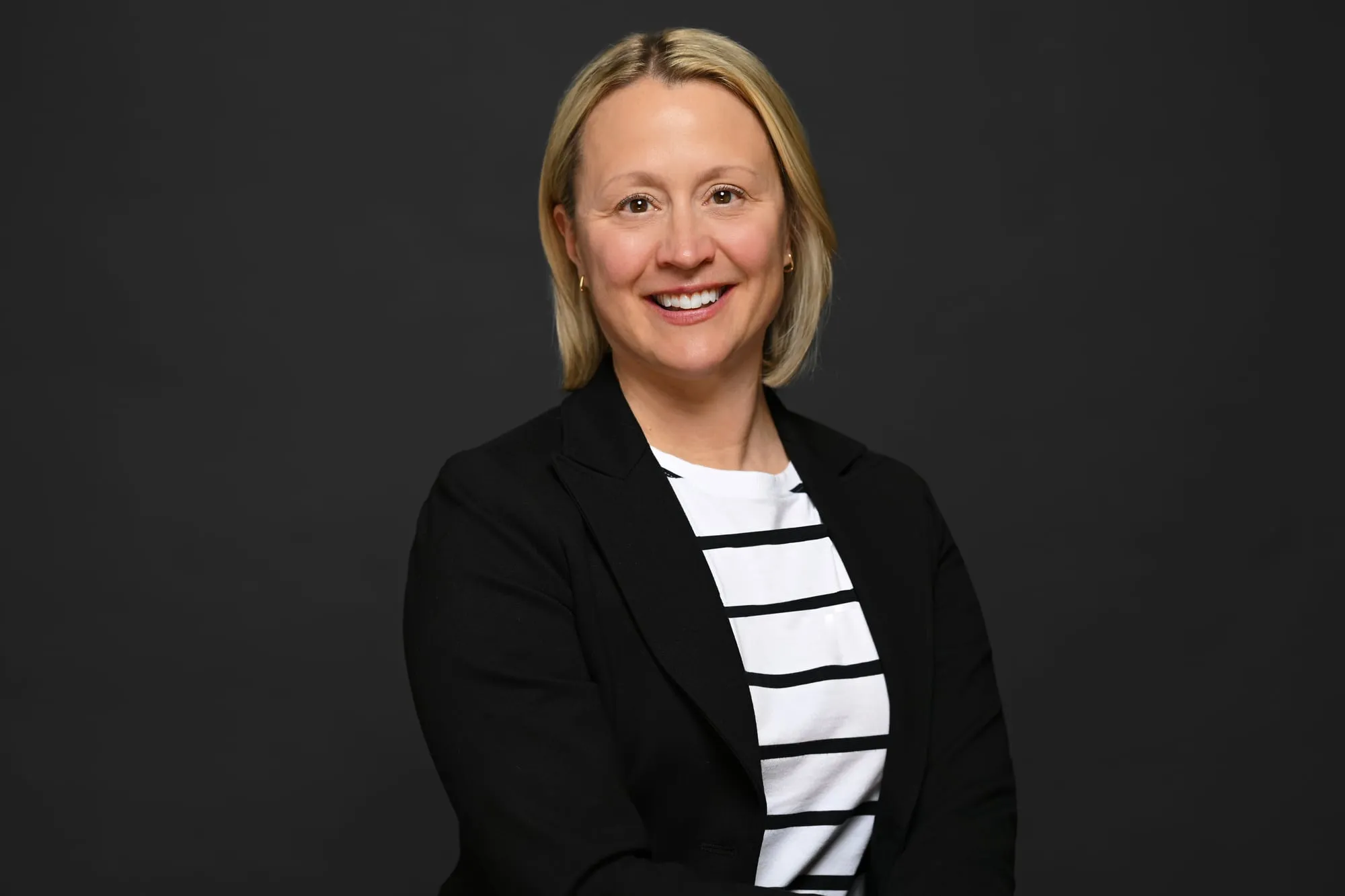 Studio headshot on a black background: black blazer over a striped top