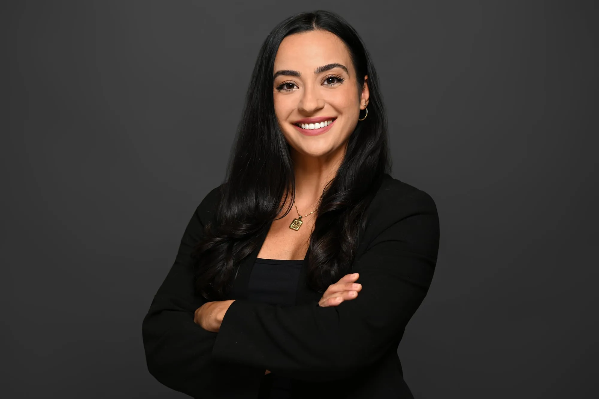 Studio headshot on a black background: black blazer, arms crossed