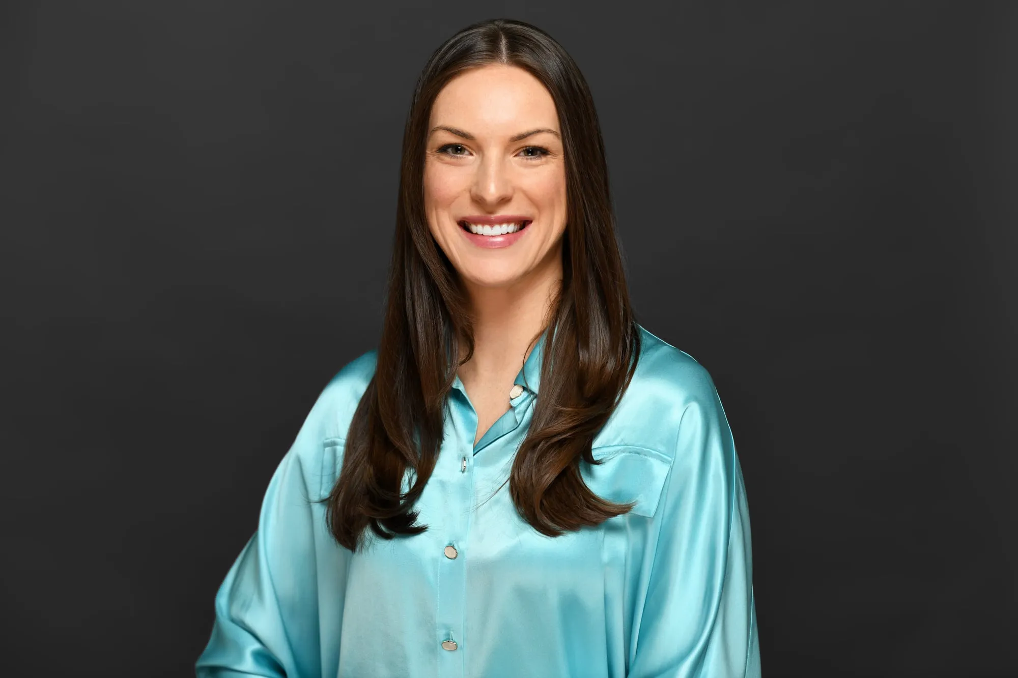 Studio headshot on a black background: aqua satin blouse