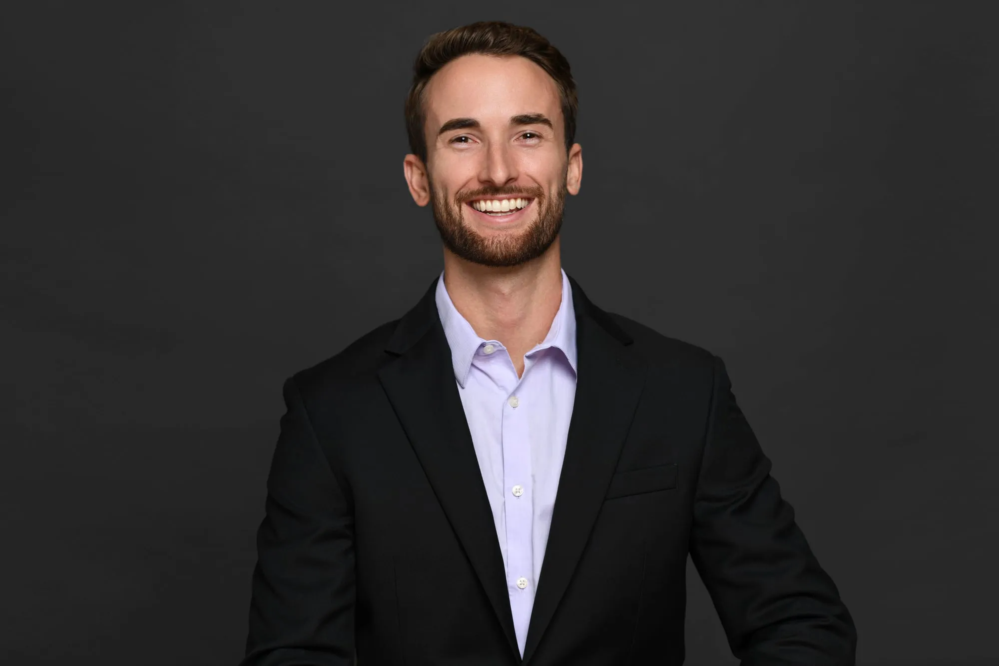 Studio headshot on a black background: black blazer and lavender shirt