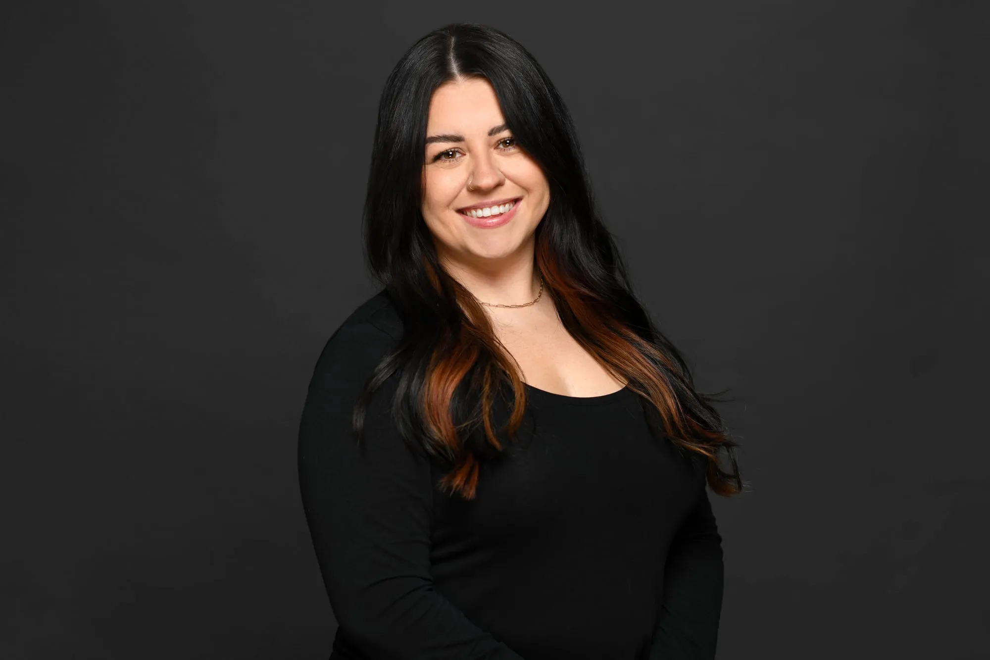Studio headshot on a black background: black top and long dark hair