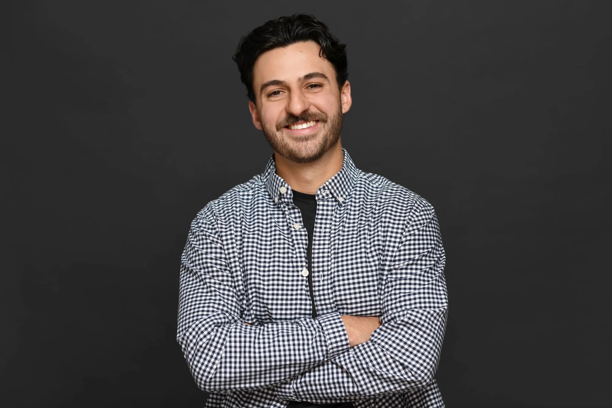 Studio headshot on a black background: gingham shirt, arms crossed