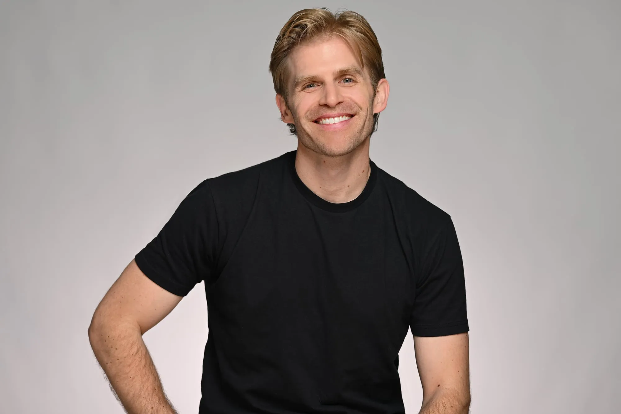 Studio headshot on a grey background: black t-shirt, relaxed and casual
