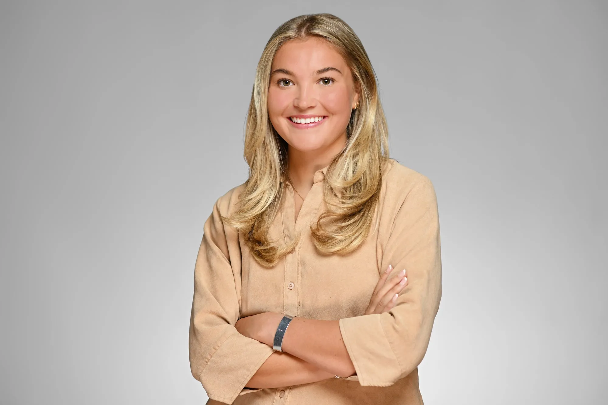 Studio headshot on a grey background: camel sweater, arms crossed