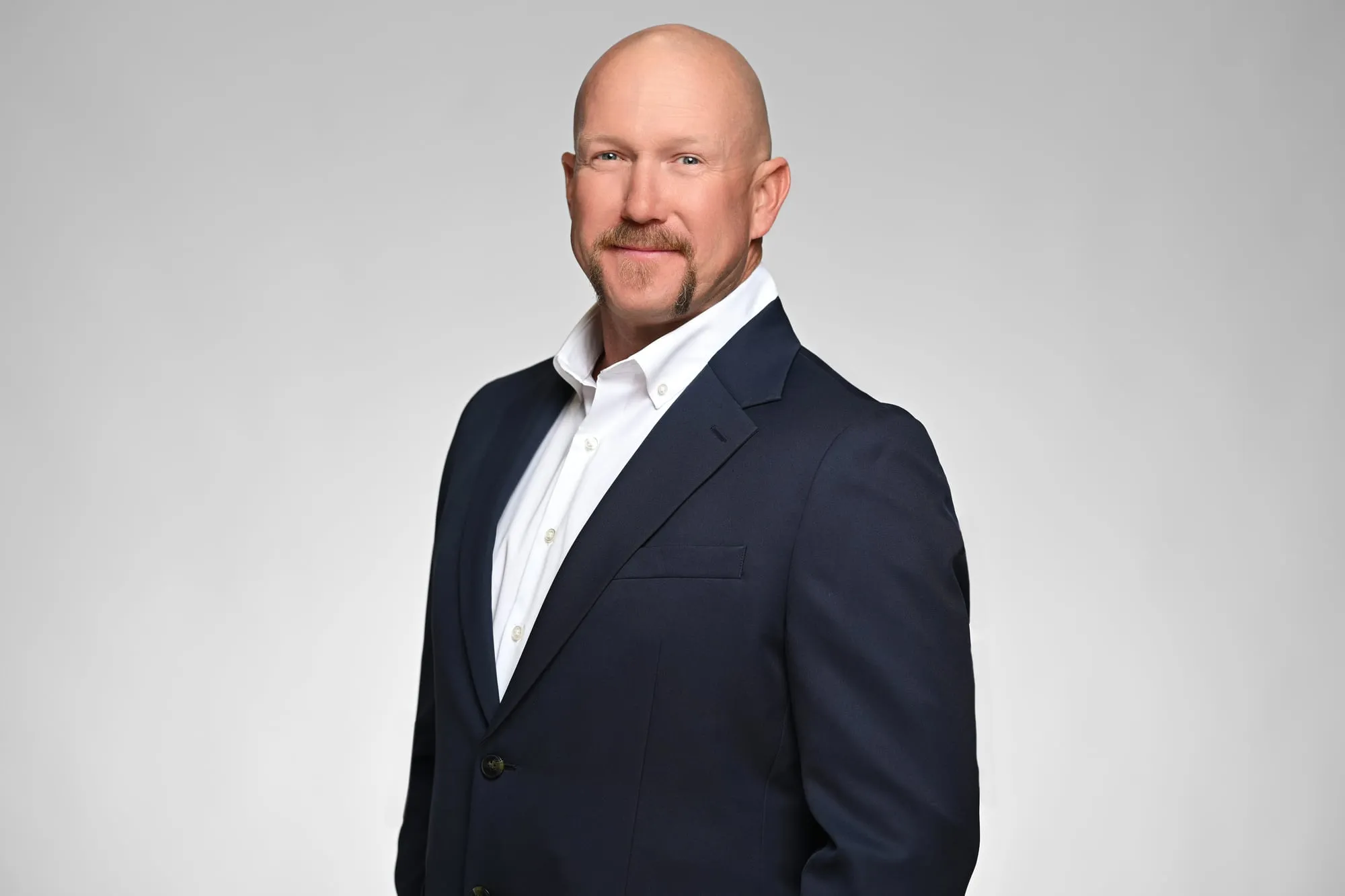 Studio headshot on a grey background: navy blazer with an open collar