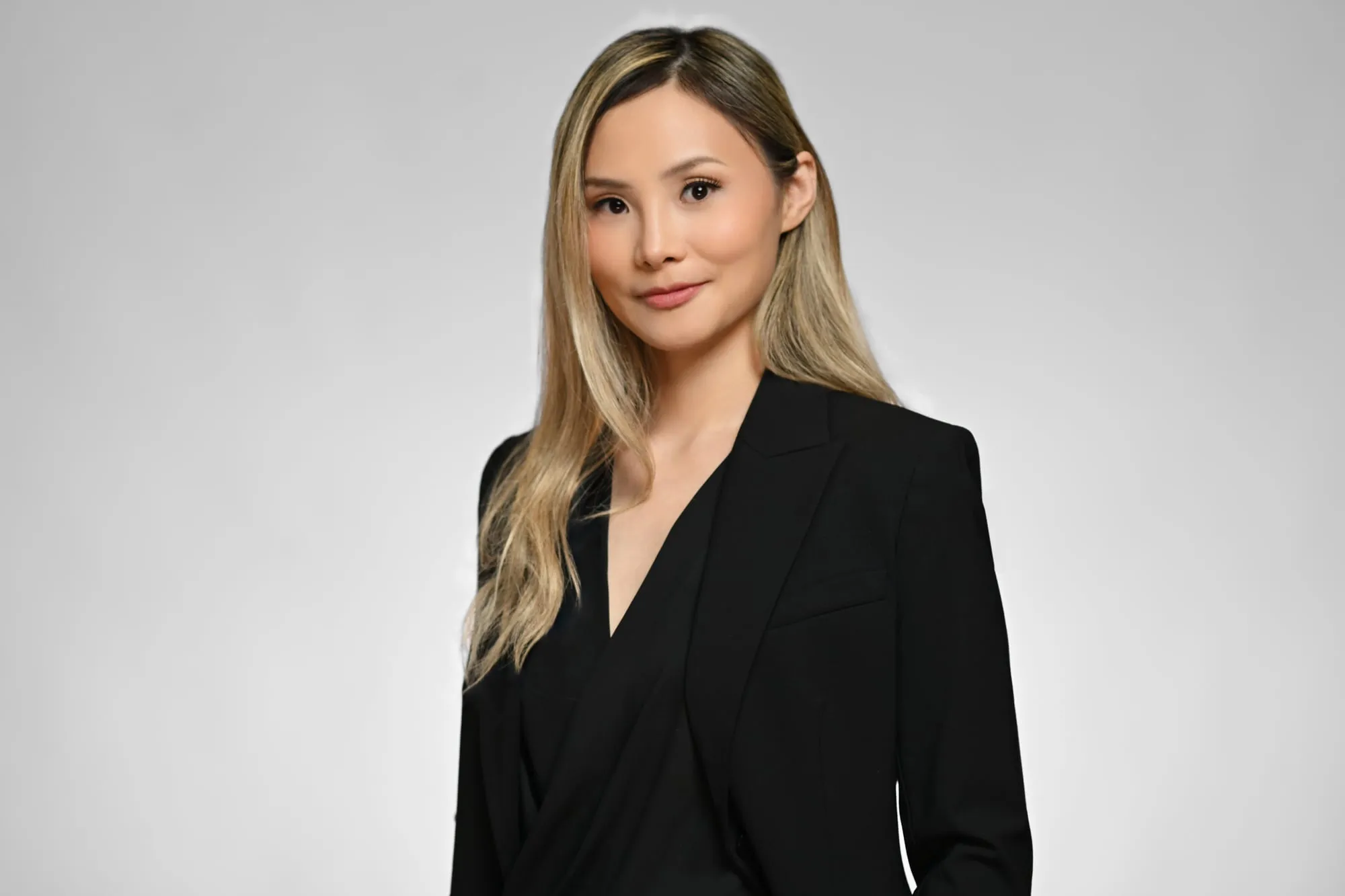 Studio headshot on a grey background: black blazer and long blonde hair