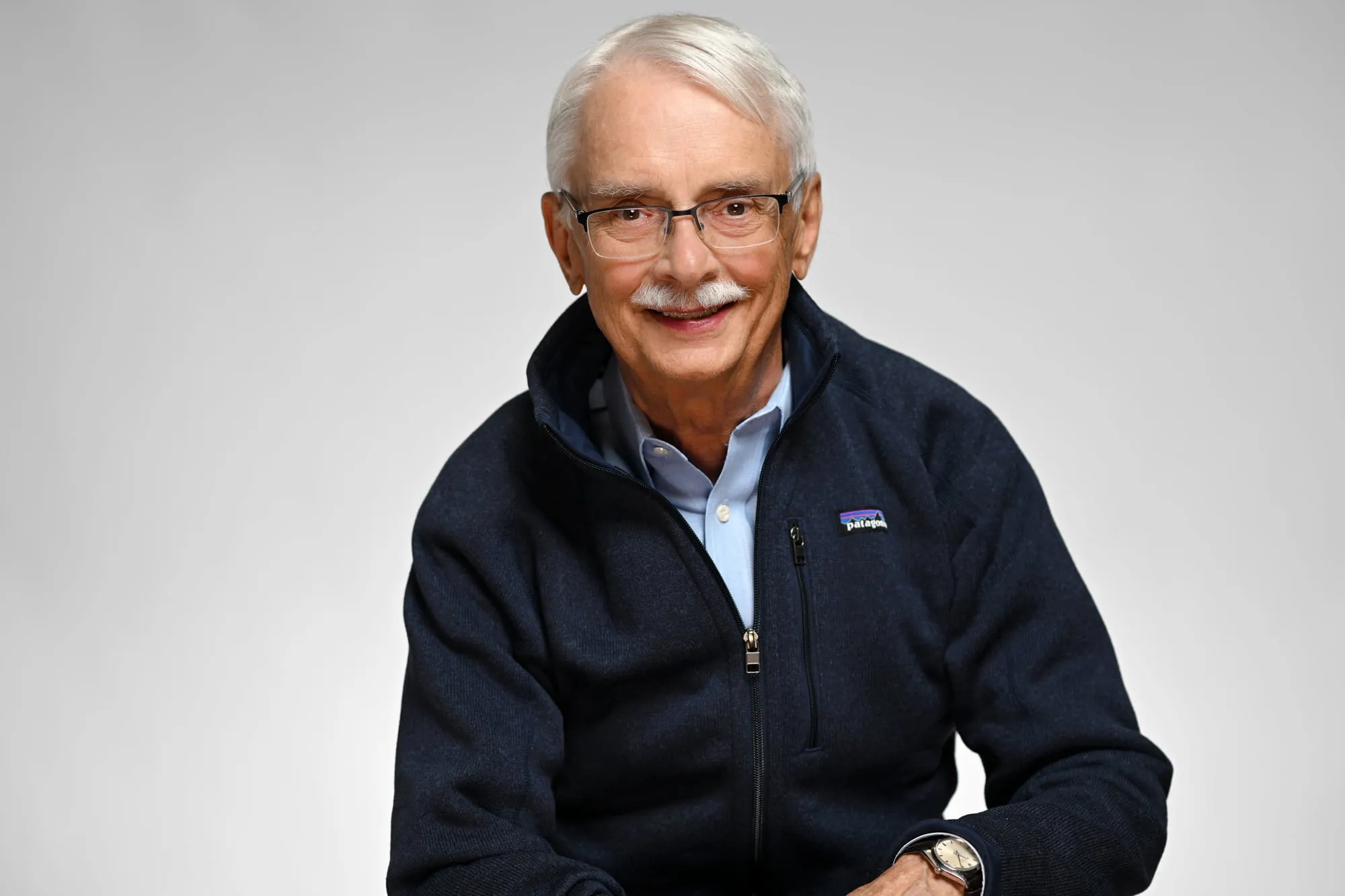 Studio headshot on a grey background: navy fleece and glasses