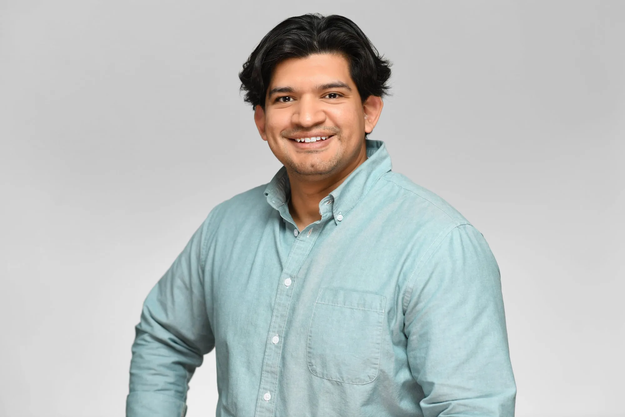Studio headshot on a grey background: mint button-up shirt