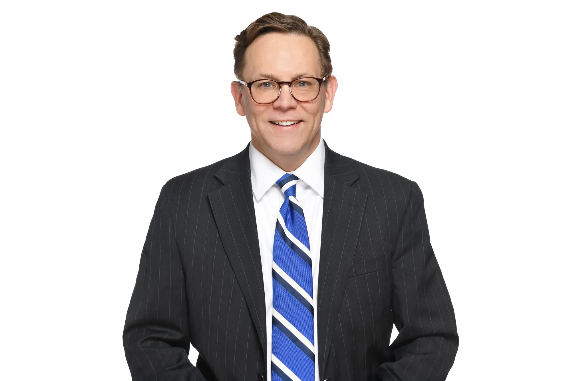 Studio headshot on a white background: charcoal pinstripe suit, glasses, and blue striped tie