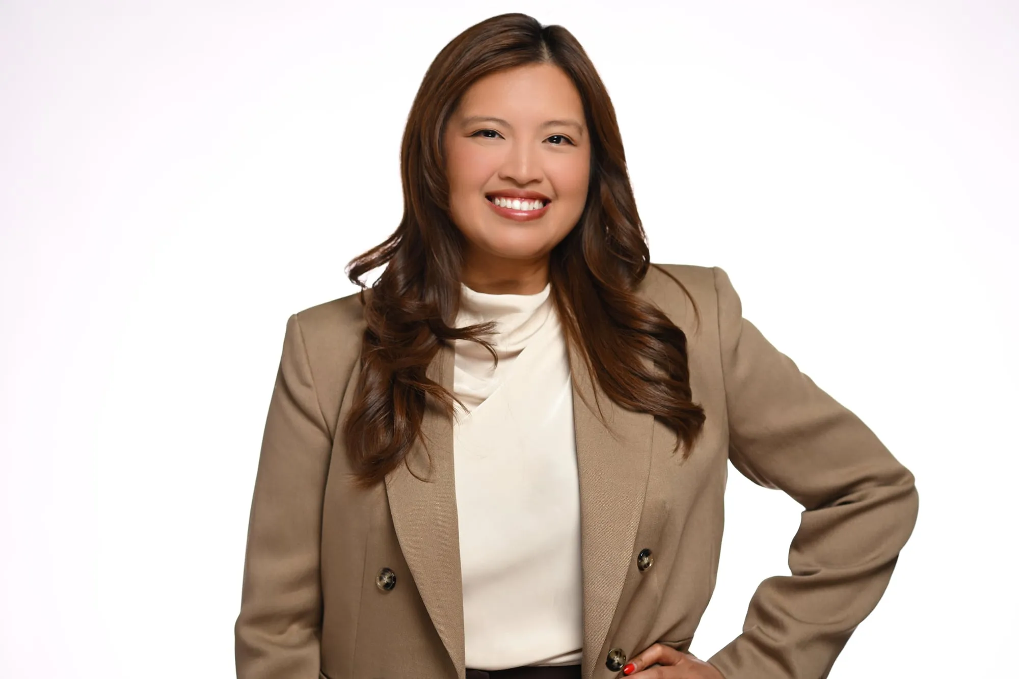 Studio headshot on a white background: camel blazer over a cream top, hand on hip
