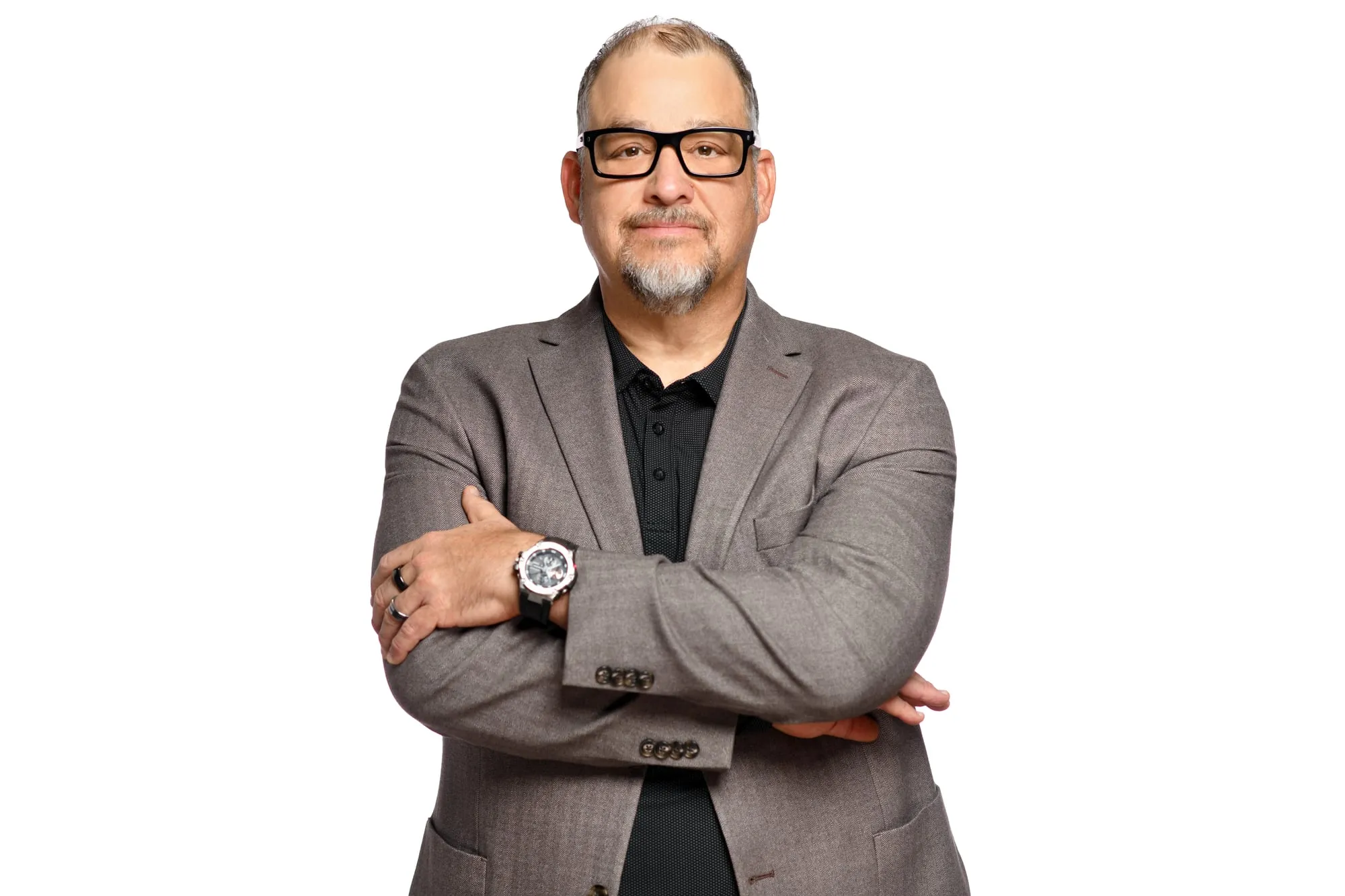 Studio headshot on a white background: grey blazer and dark-rimmed glasses, arms crossed