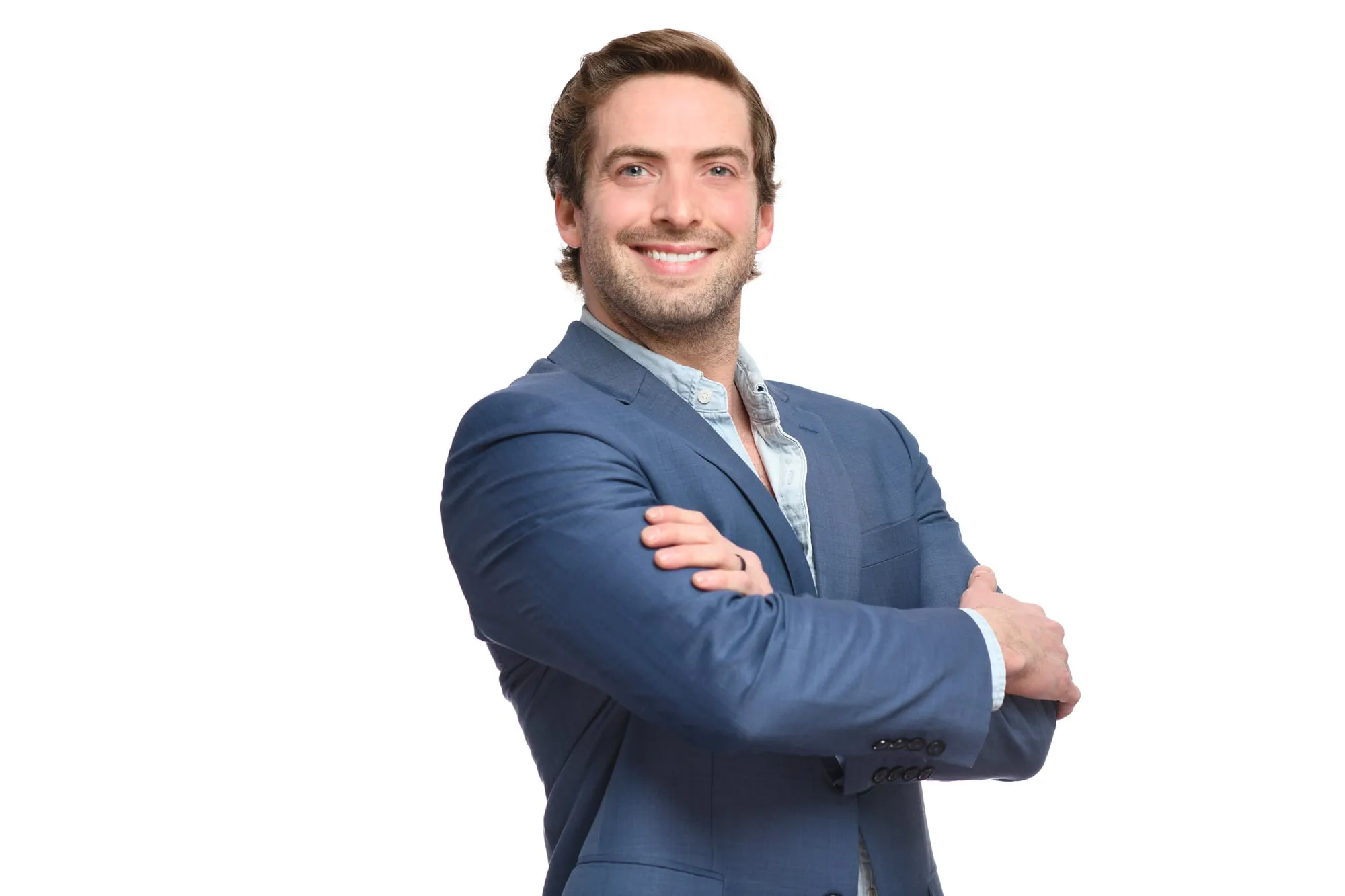 Studio headshot on a white background: blue suit with an open collar, arms crossed