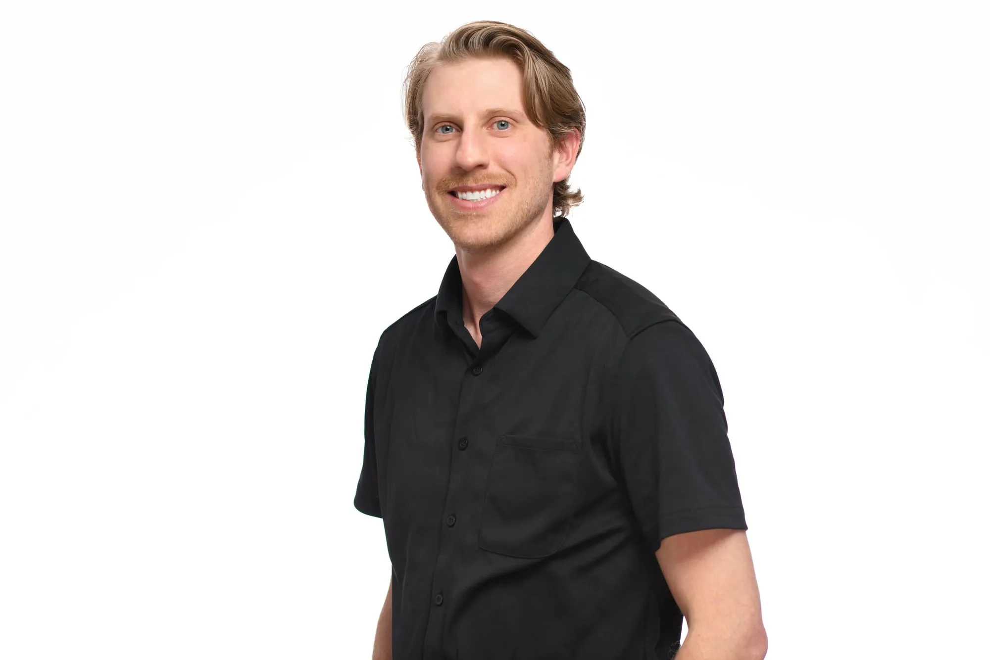 Studio headshot on a white background: black short-sleeve button-up, relaxed pose