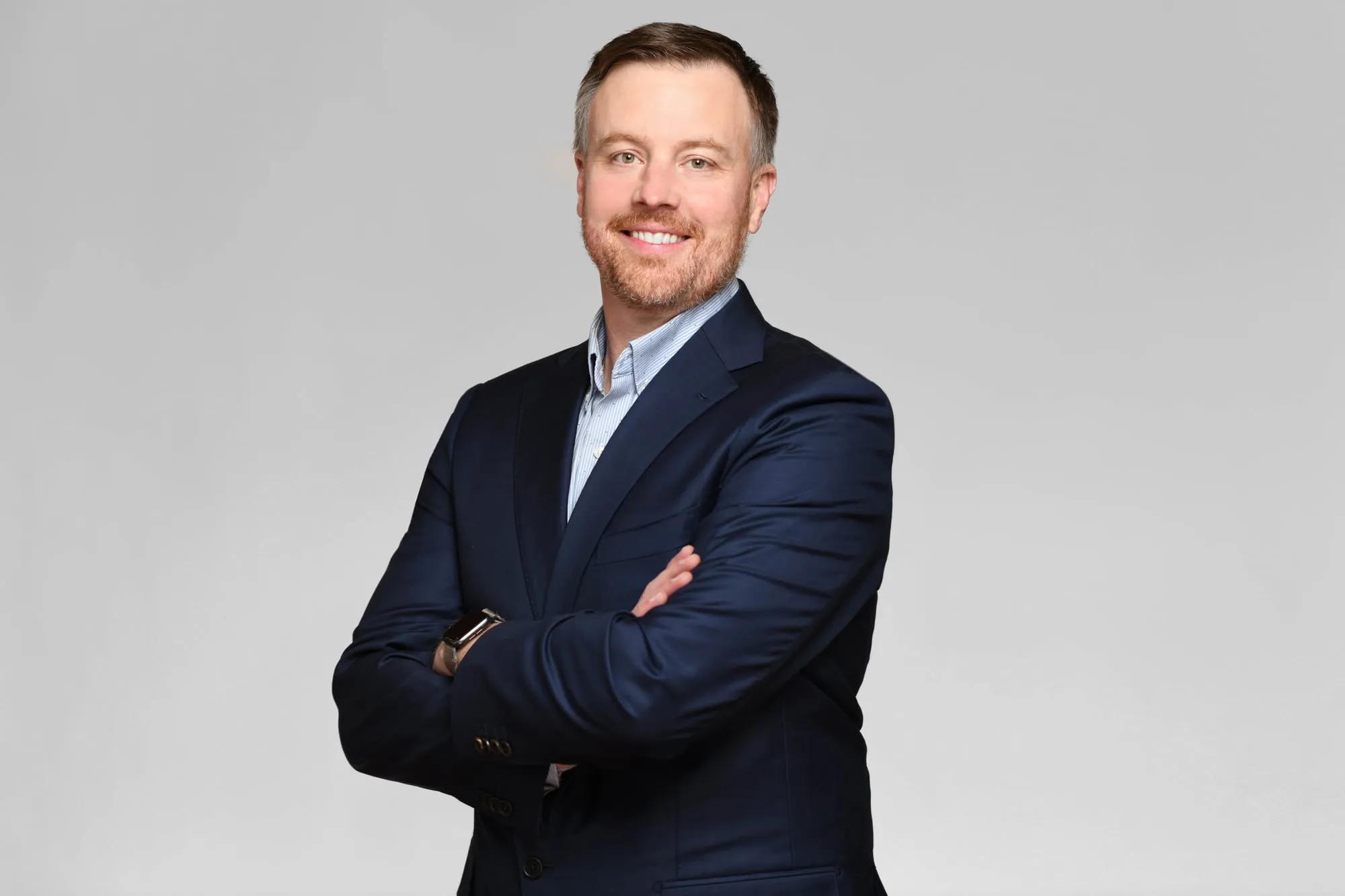 Corporate headshot for Tract in Denver on a light grey background: navy suit, arms crossed