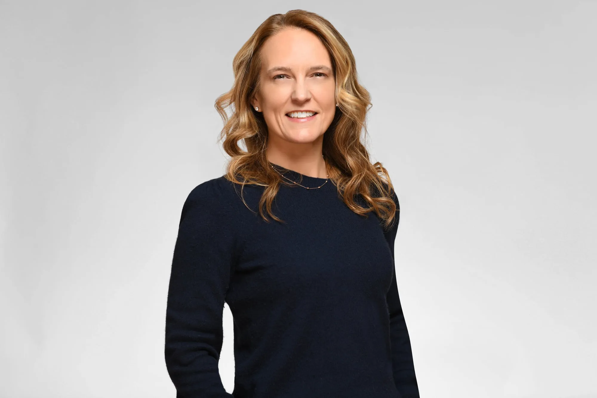 Corporate headshot for Tract in Denver on a light grey background: navy sweater