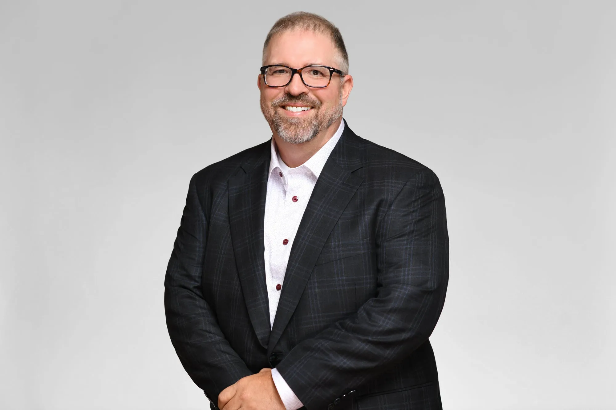 Corporate headshot for Tract in Denver on a light grey background: charcoal plaid blazer and glasses