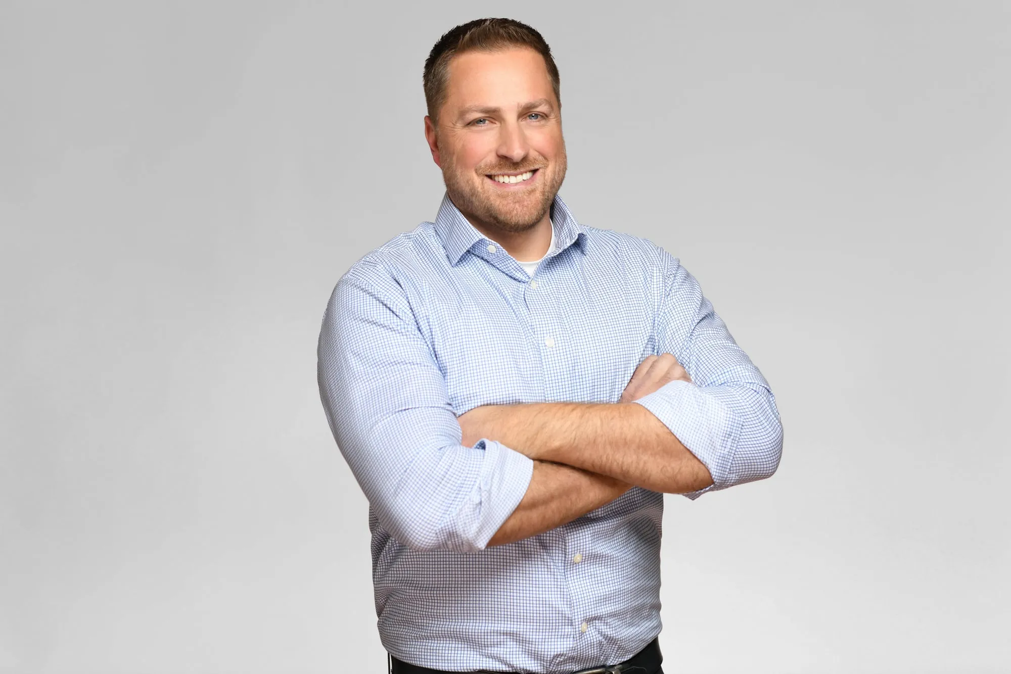 Corporate headshot for Tract in Denver on a light grey background: light blue button-up shirt, arms crossed