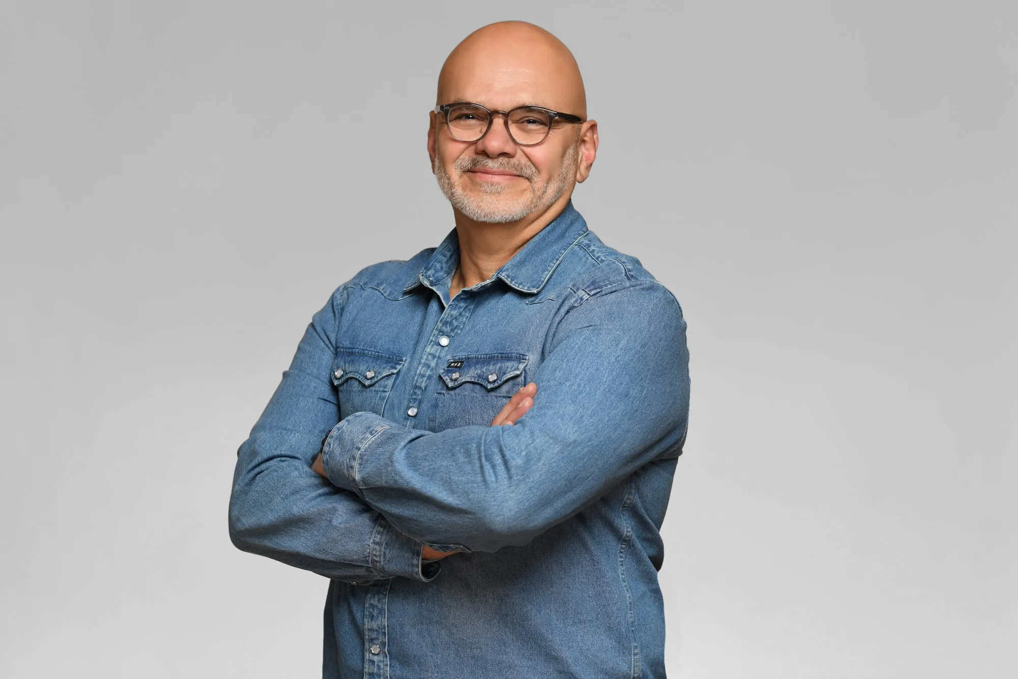 Corporate headshot for Tract in Denver on a light grey background: denim shirt and glasses, arms crossed